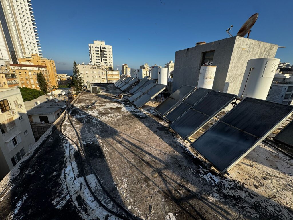 גג ישן בנתניה לפני ביצוע איטום גג עם דודי שמש – מצב של זפת סדוקה וקולטים תקועים