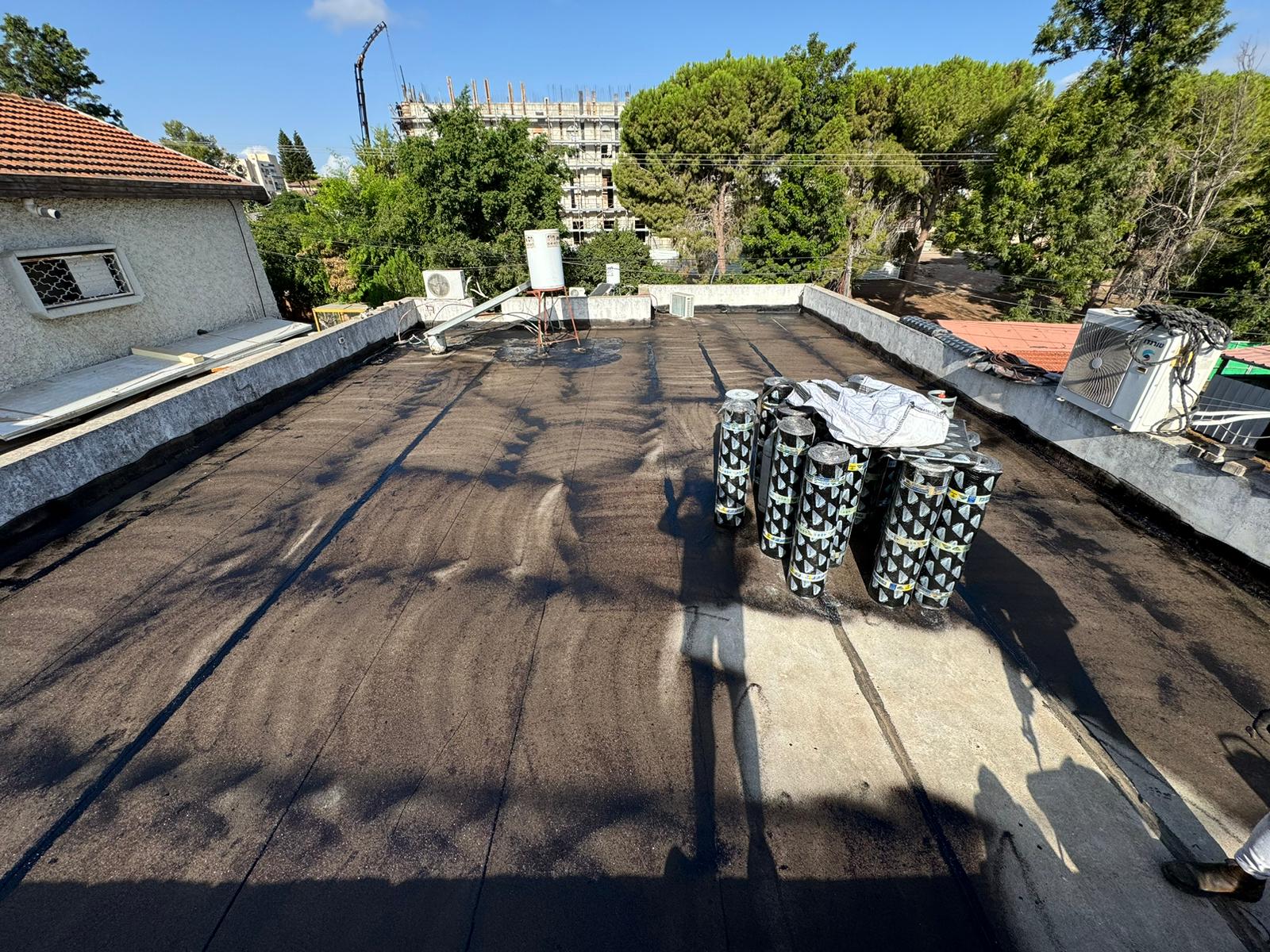 גלילי איטום ביטומן מסודרים על גג נקי בעפולה עילית לפני התחלת עבודת האיטום