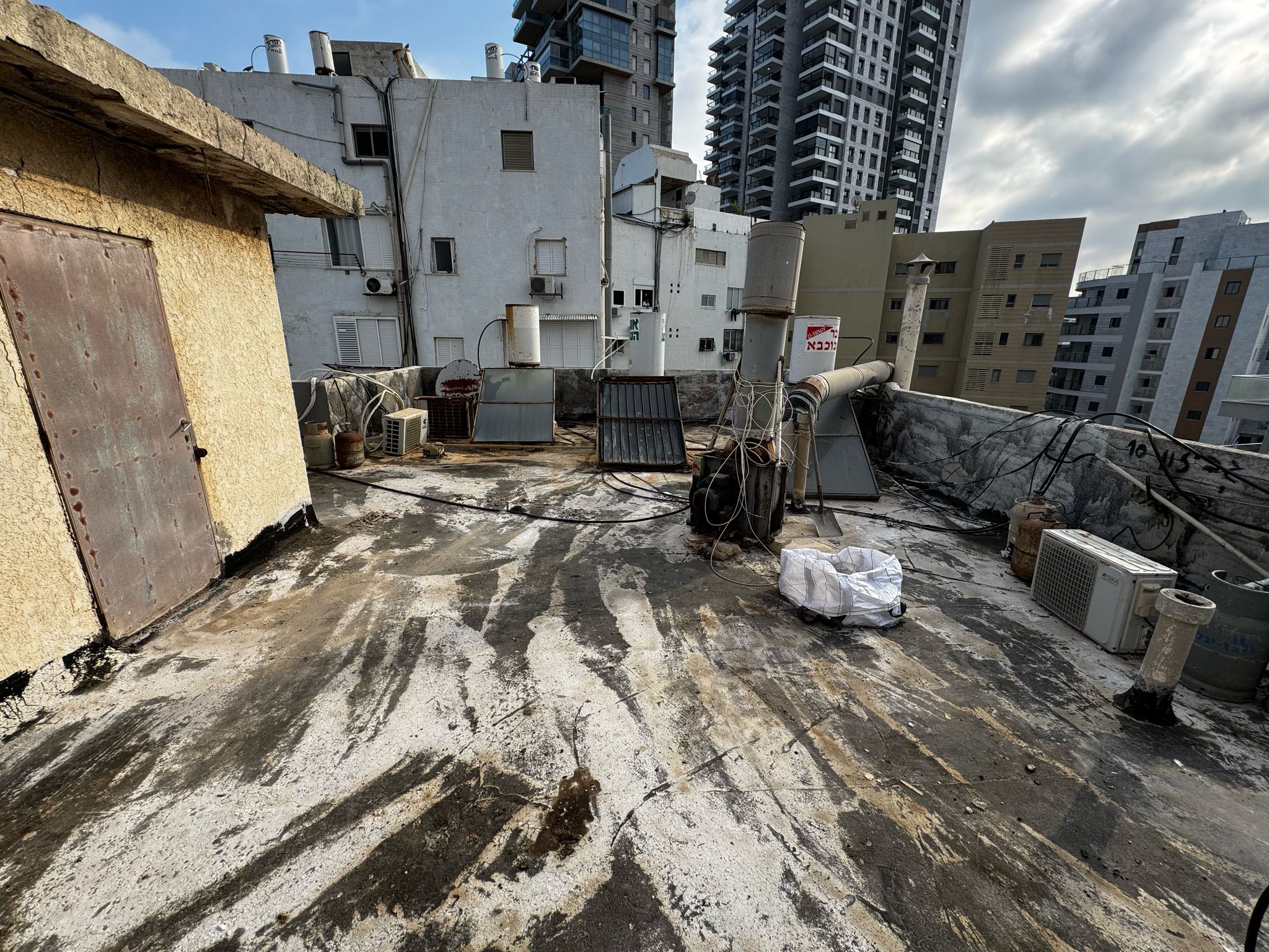 מרפסת ישנה לפני איטום בחיפה עם שאריות חומרים, לכלוך ומערכות שמש, לקראת פרויקט שיקום מלא